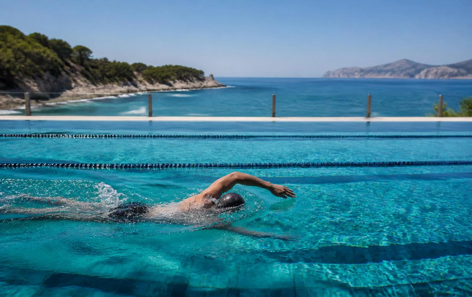 Sportlicher Schwimmer in einem Bahnenbecken über einer mediterranen Bucht auf Mallorca