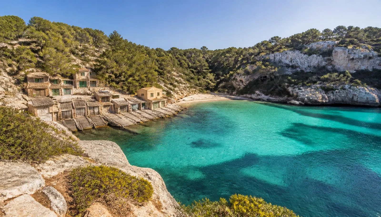 Cala Llombards auf Mallorca mit türkisfarbenem Wasser, felsiger Küste und traditionellen Bootshäusern