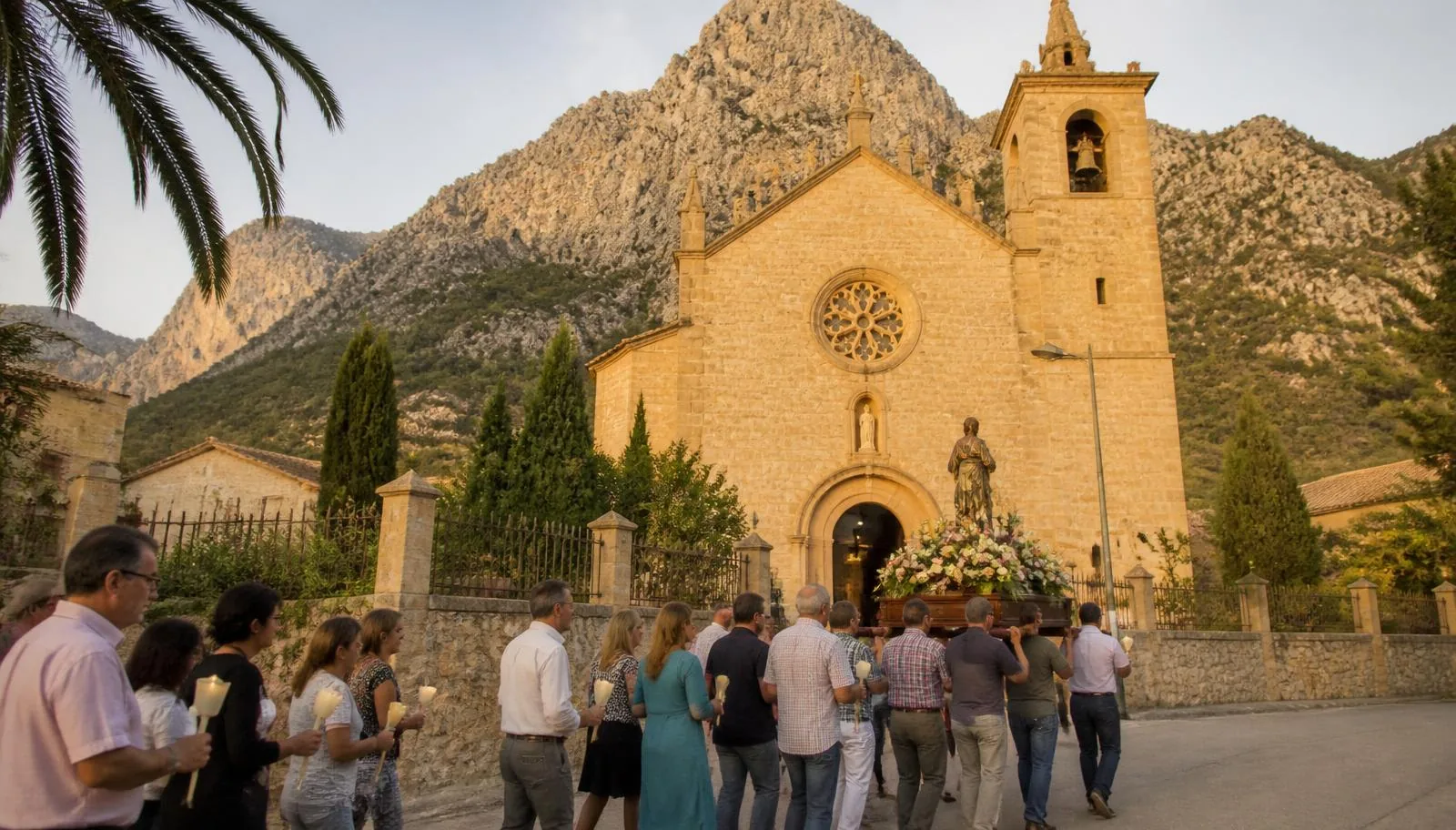 Prozession mit Kerzen und einer blumengeschmückten Heiligenfigur vor einer Dorfkirche in der Serra de Tramuntana auf Mallorca
