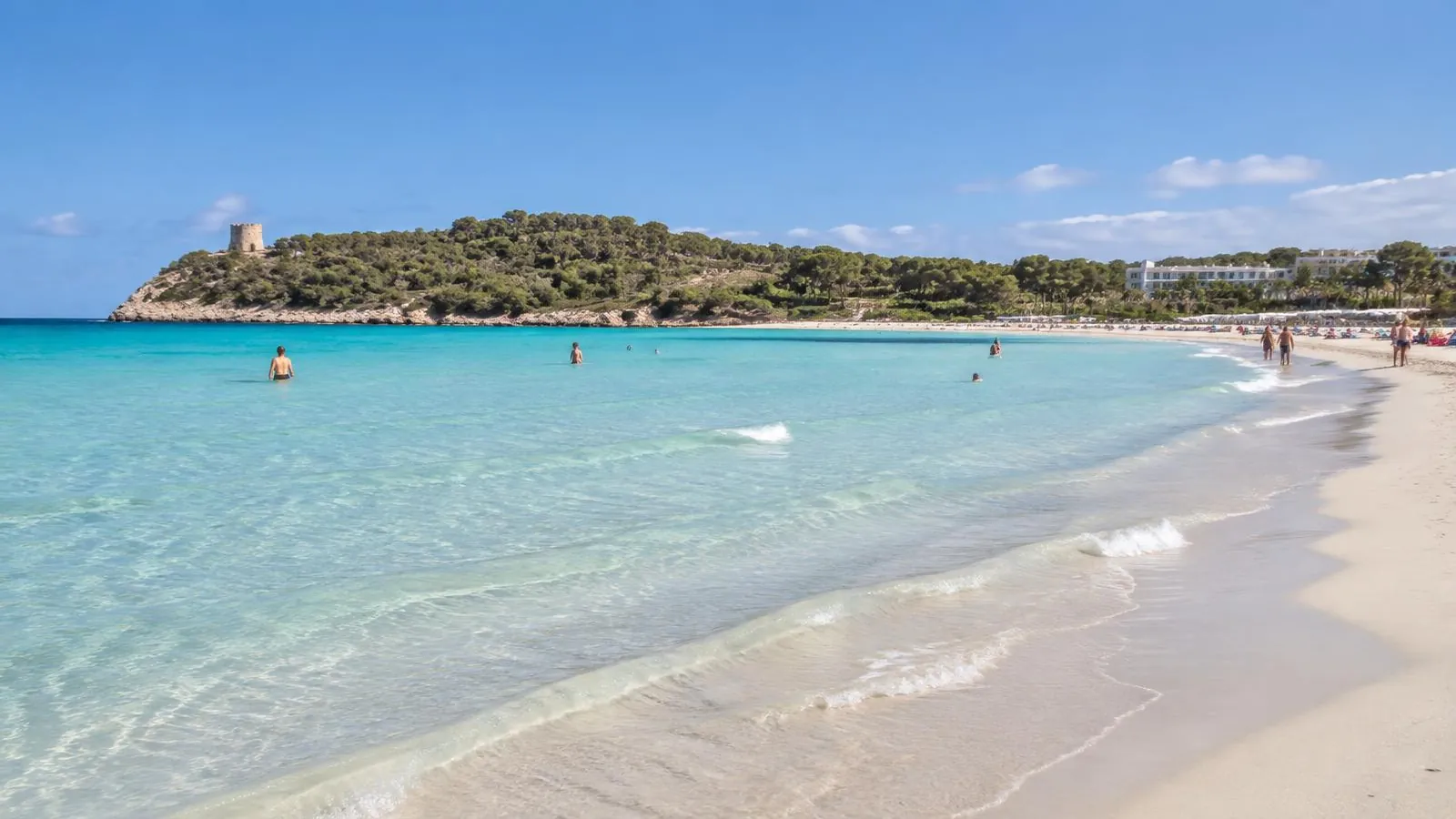 Flach abfallender Sandstrand von Sa Coma im Osten Mallorcas mit türkisem Wasser und der bewaldeten Halbinsel Punta de n'Amer